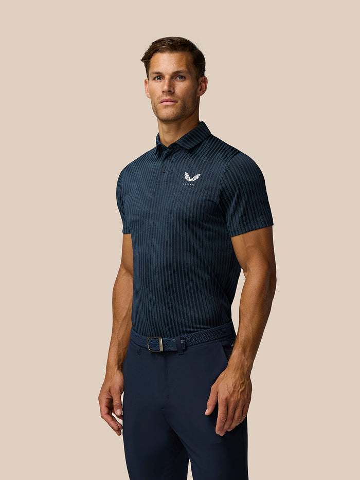 Male model wearing Midnight Navy Golf Pinnacle Glow Polo with all over stripes and Castore logo on the left chest