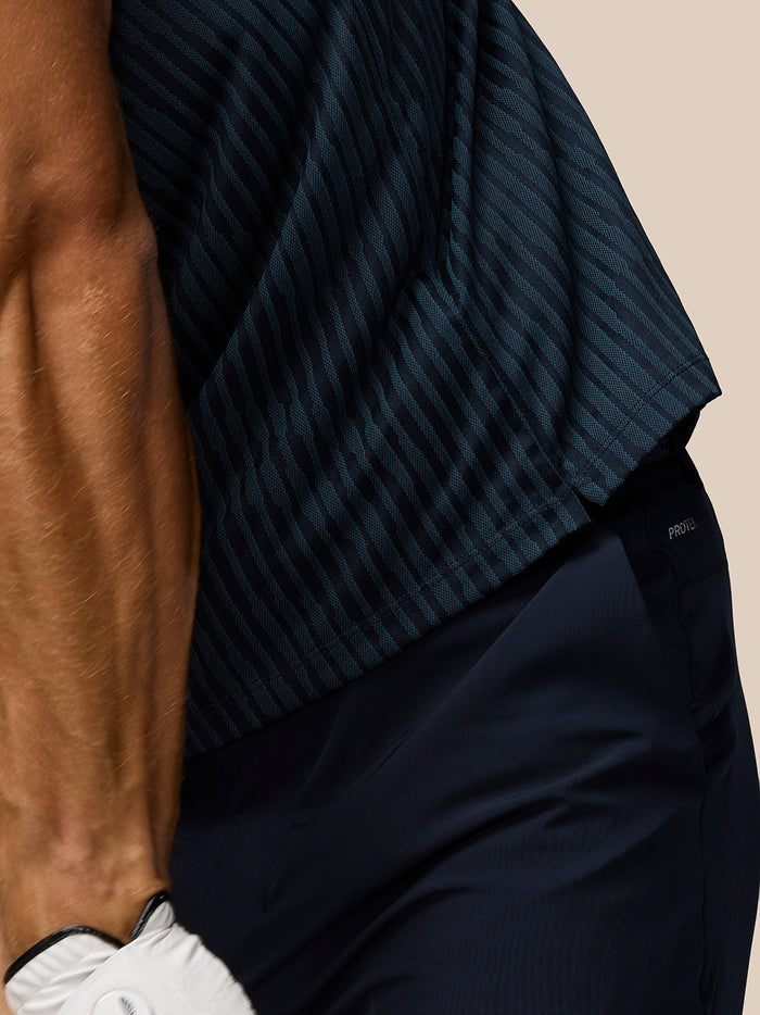 Close-up of navy striped knit fabric from the Golf Pinnacle Glow Polo with dark trousers in the frame.