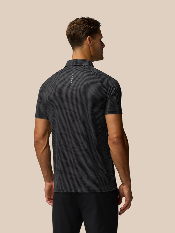 Back view of male model in dark grey printed golf polo showing pattern and vertical Castore logo on the upper back.