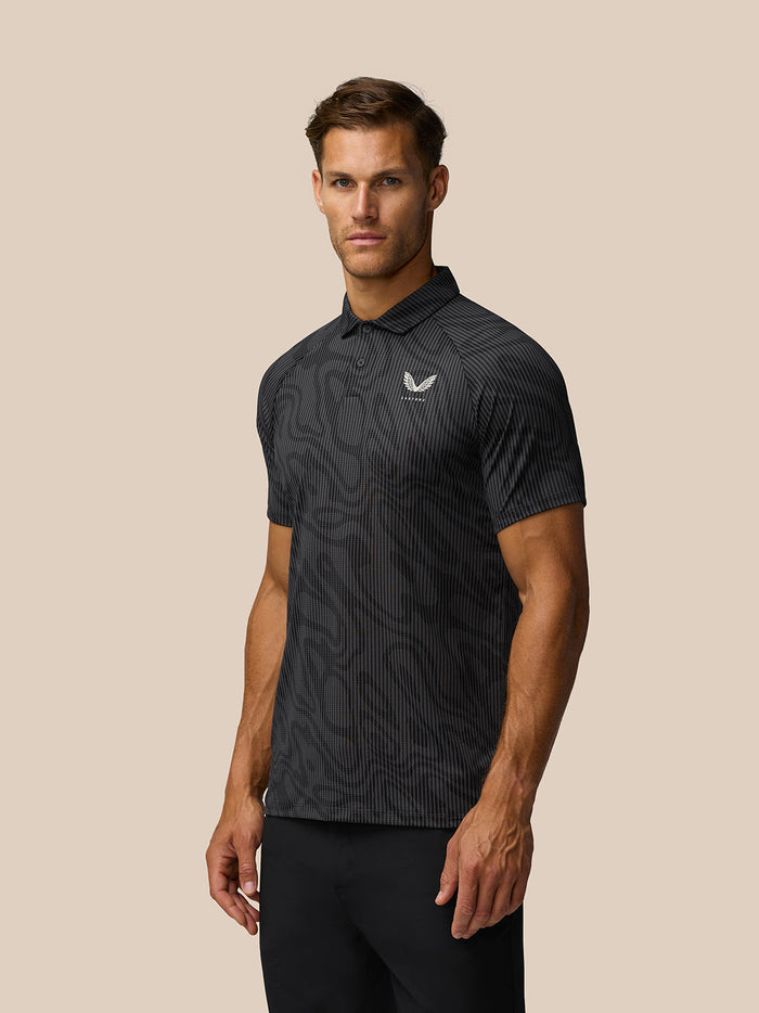 Three-quarter view of male model in gunmetal grey printed polo with Castore logo on left chest.