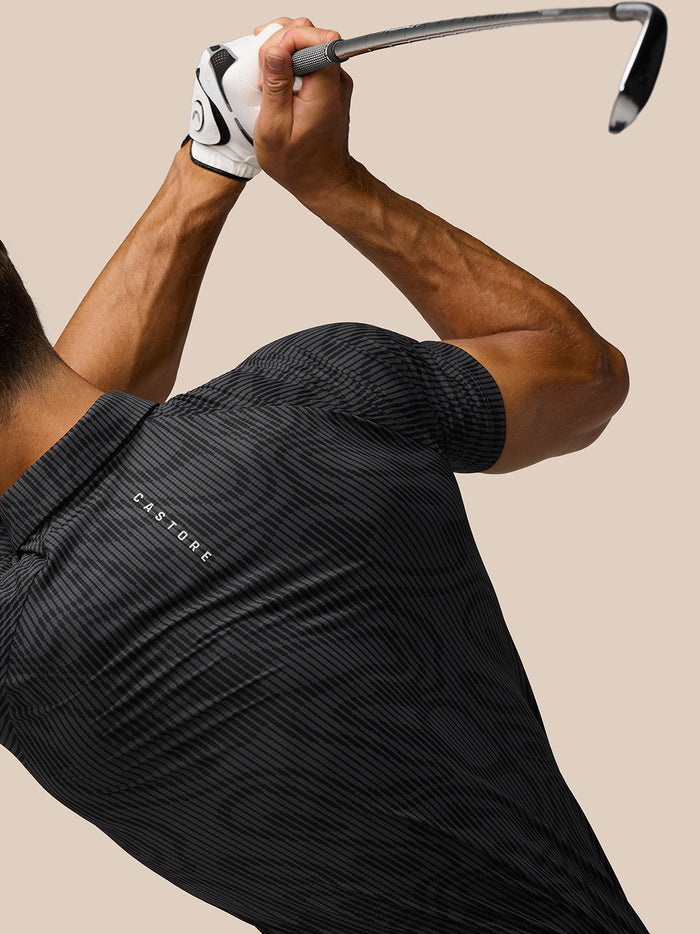 Back view of a golfer in Golf Club Glow Printed Polo gunmetal grey with Castore branding and AerTek fabric during a swing.
