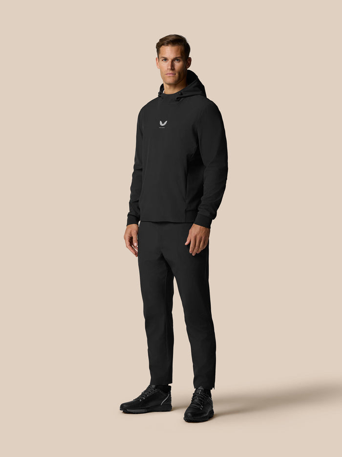 Full body view of a man in black Golf Pinnacle Performance Hoodie with hood and matching pants, Castore logo on chest