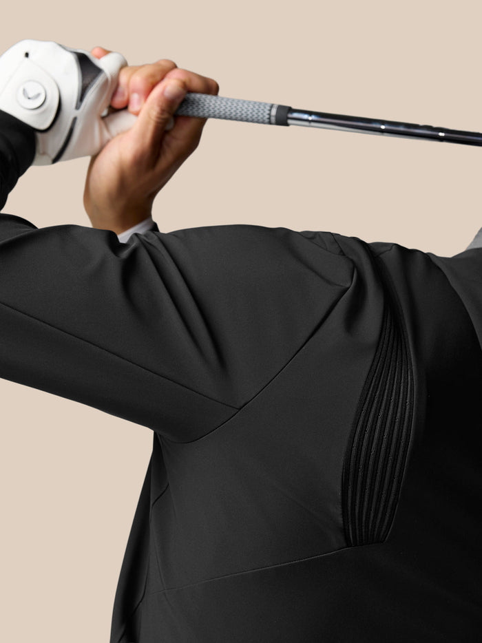Golfer in a black Pinnacle Performance Hoodie gripping a golf club during a swing