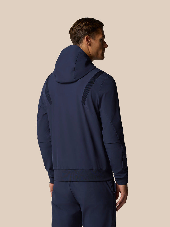 Back view of a male model wearing a midnight navy hooded golf jacket with ribbed shoulder panels.