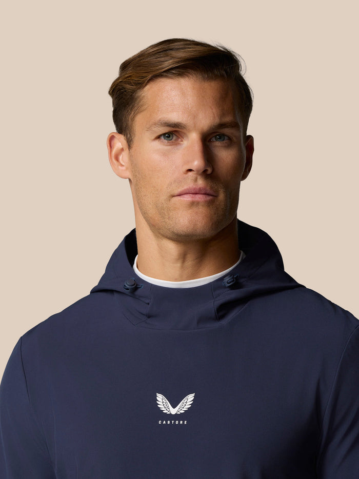 Close up of male model in navy Castore Golf Pinnacle Performance Hoodie with hood and chest logo
