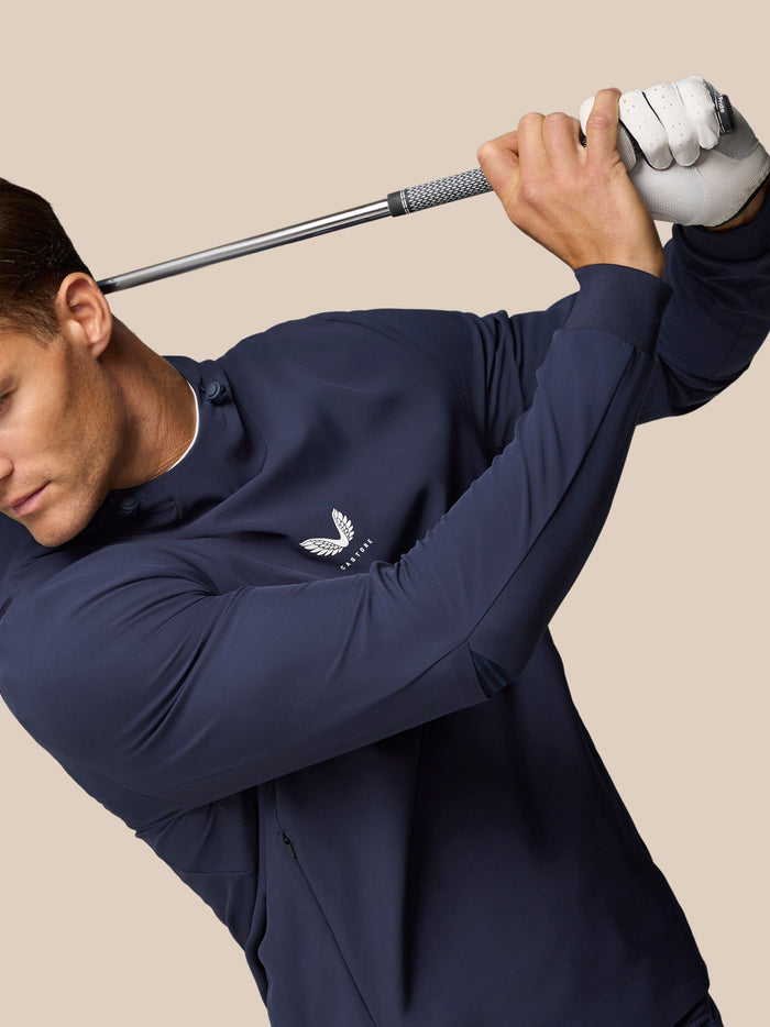 Male model in navy Castore Golf Pinnacle Performance Hoodie shown mid swing with logo on chest