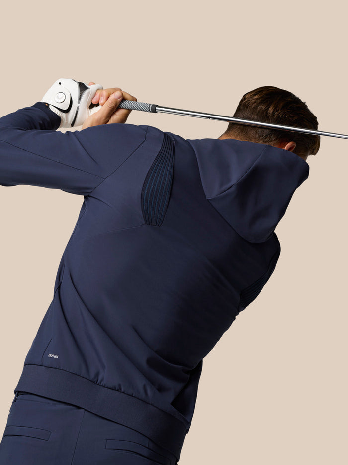 Golfer wearing midnight navy Golf Pinnacle Performance Hoodie mid swing with a golf club