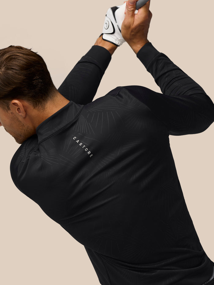 Angled back view of a man wearing the Castore Golf Club Classic 1/4 Zip Debossed Top in black with allover print
