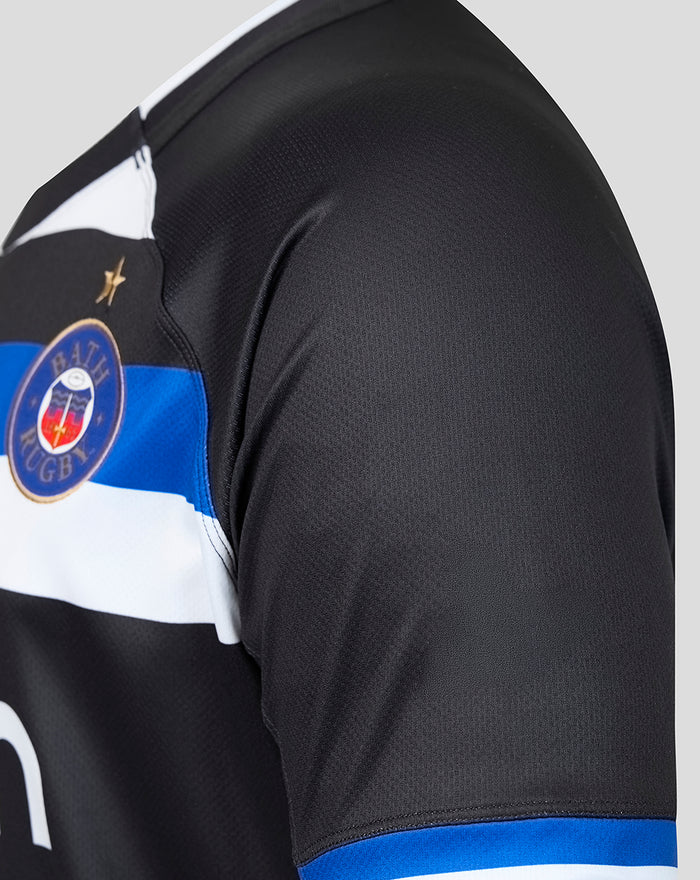 Close-up of Bath Rugby crest on black home shirt with blue stripe and fabric texture.