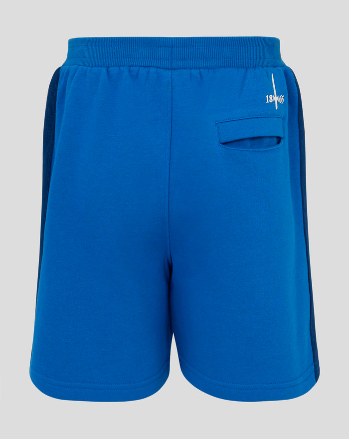 Blue junior classic shorts with white side stripe and a circular logo patch near the hem