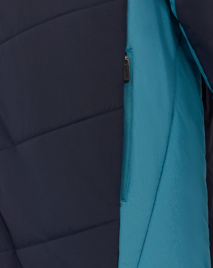 Side close-up of navy padded jacket showing teal contrasting panel and a teal zip pocket along the seam