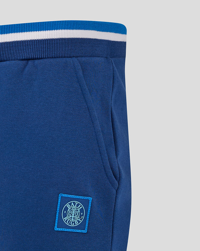 Close-up of navy jogger waist showing striped elastic waistband and a stitched logo patch near the pocket.